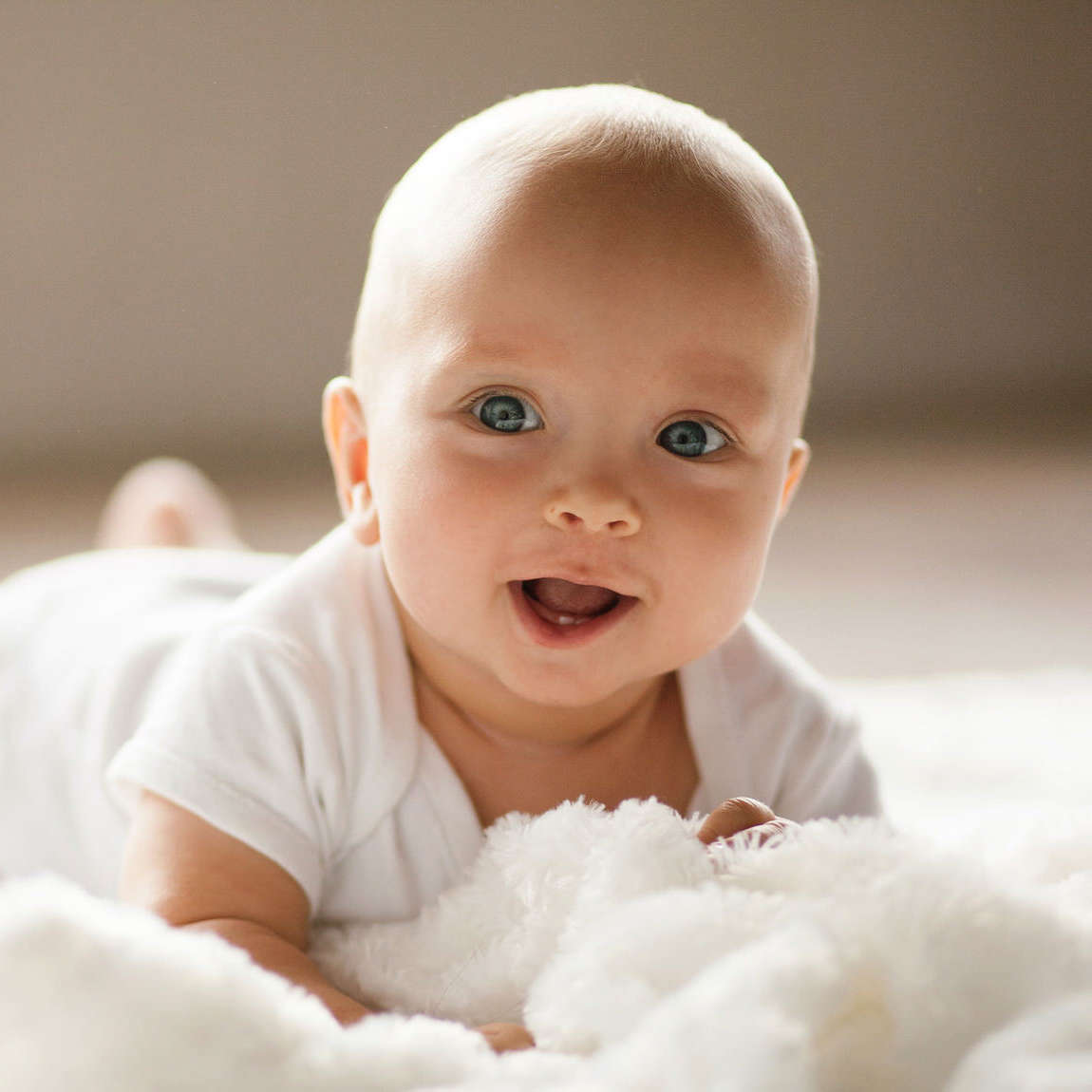 Portrait of small baby. Kid is lying, smiling and showing two teeth.
